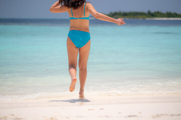 woman runs enters into the tropical beach water at sunset on white sand, surrounded by calm waves...