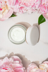 Top view of jar with face cream and pink peony flowers. Natural organic cosmetics concept