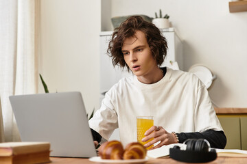 Cozy young man enjoying breakfast while focused on laptop in warm home setting