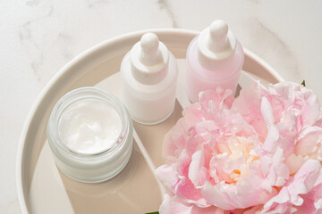 Natural organic cosmetic products with essential peony oil. Skin care cosmetics on concrete tray with flowers.