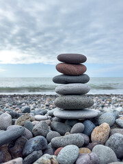 Vertical stack of zen stones on beach with cloudy sky and sea in background
