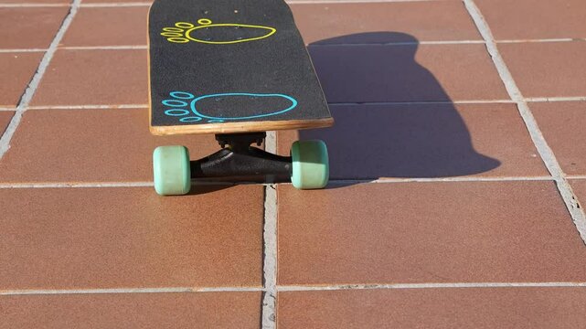 Skateboard with colorful footprint design rests on a red tiled surface, moving alone from bottom to top