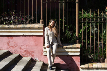 Young, pretty blonde businesswoman sitting on the wall of the porch of a house with abundant...