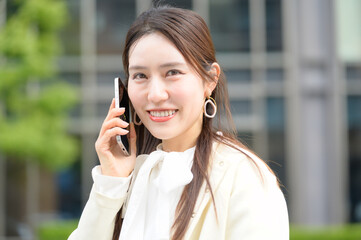 街中でスマートフォン通話をしながら微笑む白い服の女性のポートレート