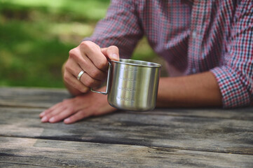 Person Holding a Stainless Steel Mug at an Outdoor Picnic Table