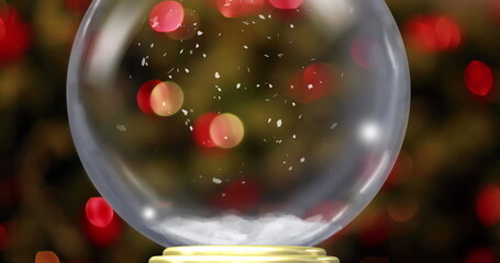 Shining glass snow globe resting on golden base in festive home, showcasing suspended snowflakes