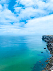 Cliffside view of the calm ocean under bright cloudy sky