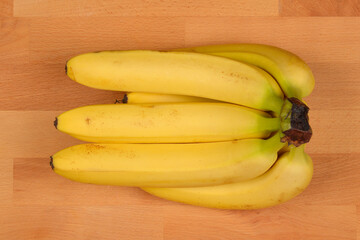 A top-down shot of a bunch of yellow bananas arranged on a wooden surface, highlighting their ripe...