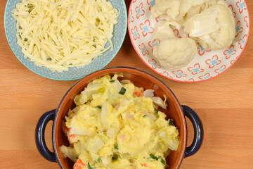 A top-down shot shows a brown oval baking dish with blue handles containing mashed potatoes and...