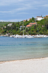 A serene coastal view of Jadranovo features boats moored in calm turquoise water near a sandy beach...