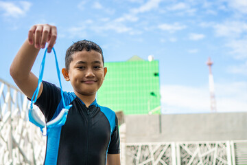 Boy Holding Swimming Goggles Smiles Outdoors on a Sunny Day