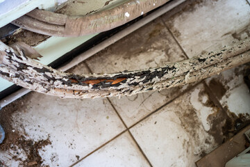 Damaged Air Conditioner Tubing with Worn Insulation on Dirty Tiled Floor