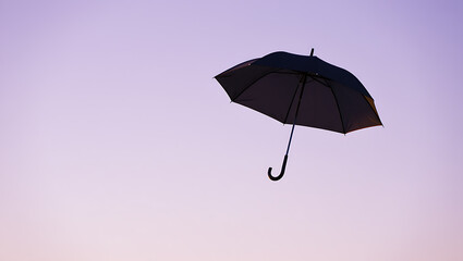 Black umbrella floating in a pastel sky