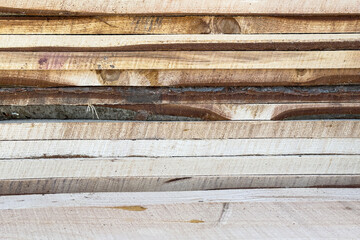 Stack of raw wooden planks with natural edges and texture, close-up view