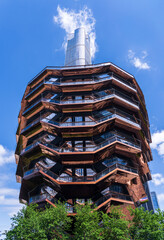 The Vessel, a unique honeycomb-shaped public landmark at Hudson Yards, stands under a bright blue sky with fluffy clouds