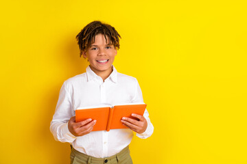 Smiling young boy in white shirt holding a bright orange book against a vibrant yellow background...