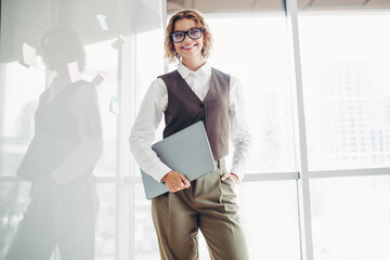 Fototapeta premium Confident businesswoman in stylish formalwear holding a laptop in an office environment