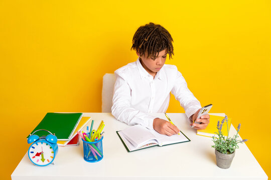 Teenage boy studying at desk with school supplies on yellow background exploring education and technology