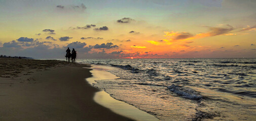 Attractive summer sunset on the beach with people riding horses in the distance.
