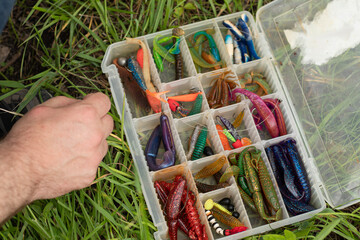 male hand With multi-colored silicone wobblers. Plugs popular type hard-bodied fishing lure. Preparation selection fishing lures. Predator catch concept. picking lures silicone baits from organizer 