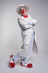 Сlown in a white coat, hat and large red patent leather clown boots. Hands crossed over chest.