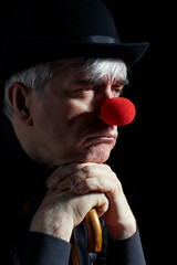 Dramatic portrait of a clown against a dark background leaning on the handle of an umbrella.