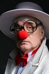 Close-up portrait of sad clown. An elderly man in a white coat and hat.
