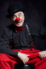 Portrait of a clown on dark background  with red clown nose and bowler hat on head.