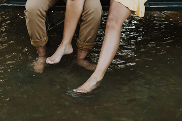 Couple dipping bare feet in shallow stream water while sitting on bench