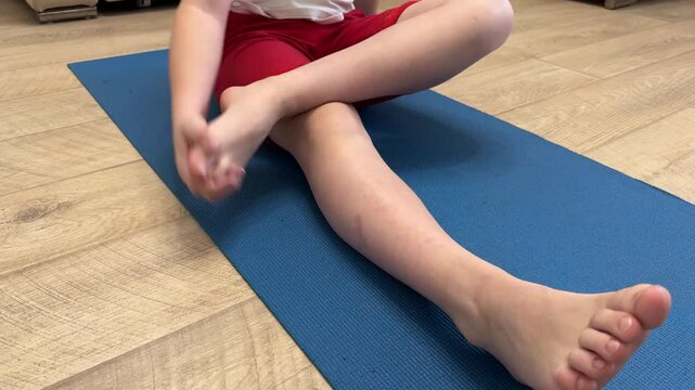 The boy does physical exercises at home on a mat with dumbbells, his own body weight and stretching.