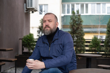 Man enjoying coffee while seated outdoors in a modern urban setting on a sunny day