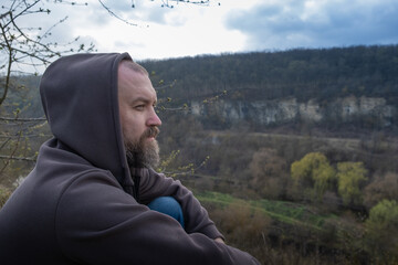 Man enjoying nature view while seated on a hillside near a river with cliffs in the background...