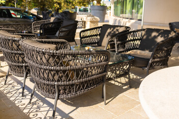 Outdoor wicker chairs with cushions in sunny cafe terrace. Modern outdoor seating, cozy atmosphere, and leisure lifestyle.