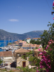 Pink blooming oleander in foreground of Fiskardo village and marina under clear blue summer sky.