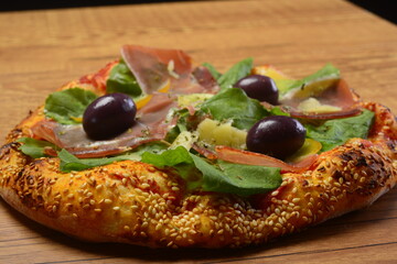 Pizza de rúcula com presunto cru e parmesão. Borda de gergelim