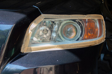 Shiny black car undergoing polishing with attention to headlight restoration. The vehicle is in a...
