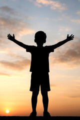 Fototapeta premium Silhouette of a Boy Praising with Open Arms at Sunrise Child Expressing Joy and Faith During Sunset