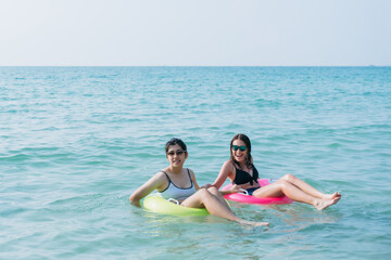 Fototapeta premium A group of carefree teenagers laughing and playing in the sea with colorful inflatable swim rings, capturing the essence of youthful joy, friendship, and summer fun by the sea.