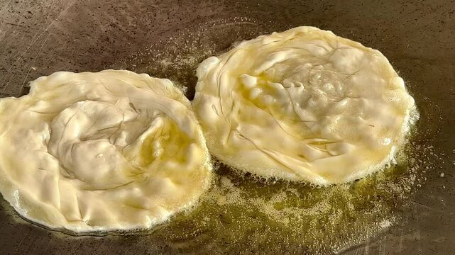 4k Street food vendor is preparing the dough and pan-frying paratha roti in hot oil until crispy on the outside. Street hawker preparing prata bread or roti canai for morning breakf