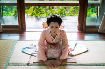 Pretty geisha or maiko Japanese woman in traditional kimono or yukata costume sitting and bowing in...