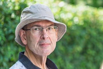 Mature man with an unshaven face sits outside looking at the camera with room for copy and dappled...
