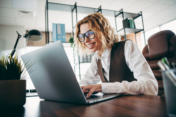 Young businesswoman working on laptop in a modern office, showcasing professional attire and...