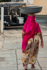 Woman carrying heavy metal bowl on head in Udaipur, India