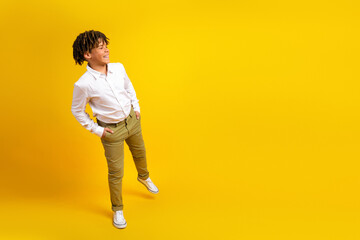 Smiling schoolboy in a white shirt posing against a bright yellow background, representing...