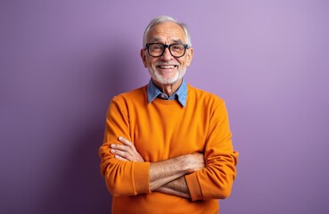 Fototapeta premium Happy elderly man smiles, arms crossed, wearing eyeglasses. Grey haired senior has positive, optimistic mood. Smiling pensioner in orange sweater, casual fashion. Portrait on violet backdrop.