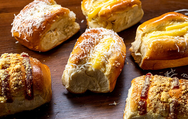 
Varieties of sweet breads.
(Vanilla cream sweet bread, guava jam with sweet flour, vanilla cream with coconut), typically Portuguese-Brazilian bread, on a rustic wooden board and black background