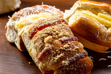 
Varieties of sweet breads.
(Vanilla cream sweet bread, guava jam with sweet flour, vanilla cream with coconut), typically Portuguese-Brazilian bread, on a rustic wooden board and black background