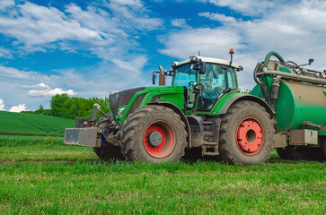 Obraz premium Agricultural machinery tractor standing in field. Large tractor. Side view. White cumulus clouds in background.