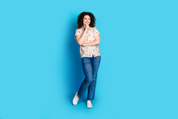 Fototapeta premium Lovely young woman with curly hair posing in casual outfit against solid blue background in contemporary relaxed style