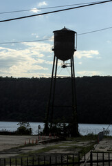 backlit tall water tower in hastings on hudson river with palasades cliffs mountains background black tank metal elevated drinking liquid